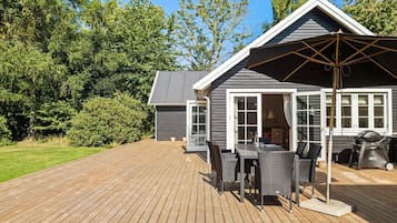 En træterrasse med udendørs møbler, grill og en overdækket patio.