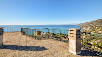 A terrace with a view of the sea, a stone balustrade, and a tiled floor.