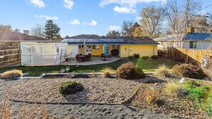 Una casa residencial con patio trasero cercado, un patio con mobiliario exterior y una pequeña área ajardinada.