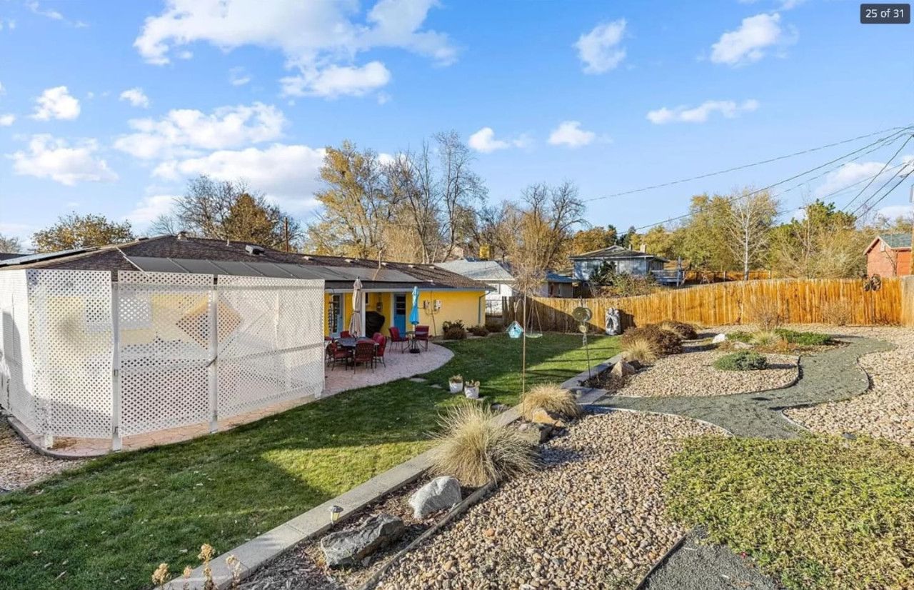 Un patio trasero cercado con área de patio, una casa amarilla y una valla de madera.
