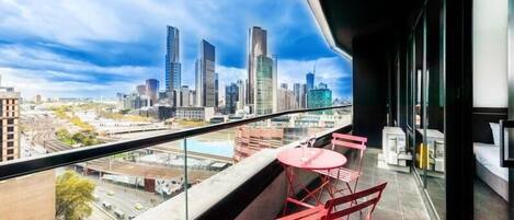 Un balcon avec vue sur la ville, des chaises rouges et une petite table.