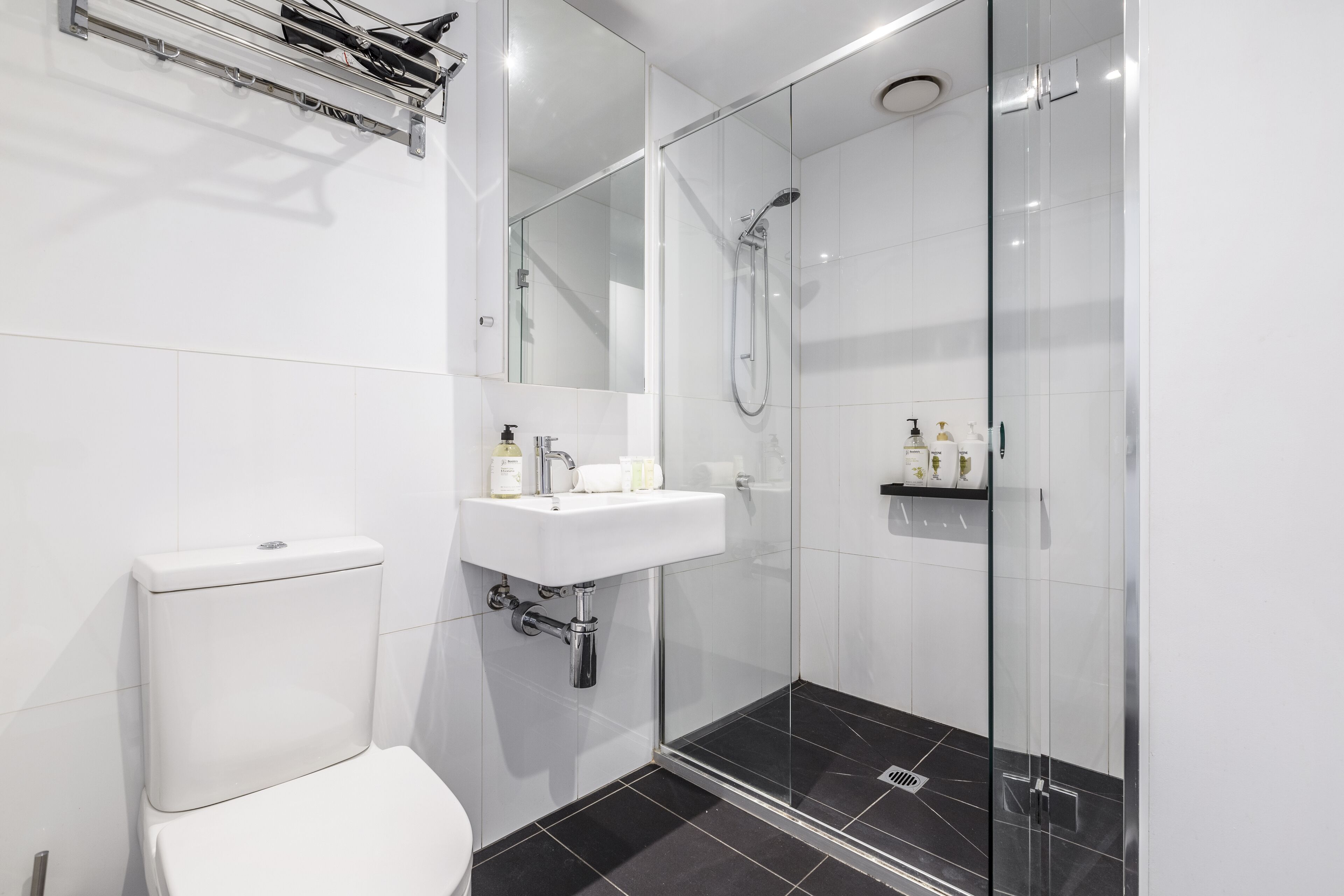 A modern bathroom with a glass-enclosed shower, a white toilet, and a sink with toiletries.
