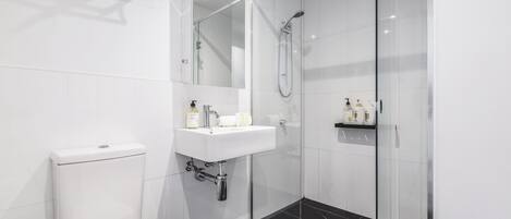 A modern bathroom with a glass-enclosed shower, a white toilet, and a sink with toiletries.