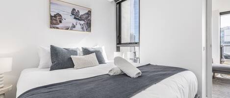 A neatly made bed with a view of the city through a large window.