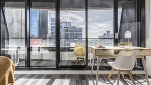 A modern room with a large sliding glass door leading to a balcony, a wooden desk with a chair, and a white lamp. - Riverview Suites by EdgeTrip (Melbourne)