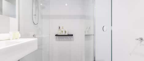 A modern bathroom with a glass shower enclosure, a white sink with toiletries, and a black tiled floor.