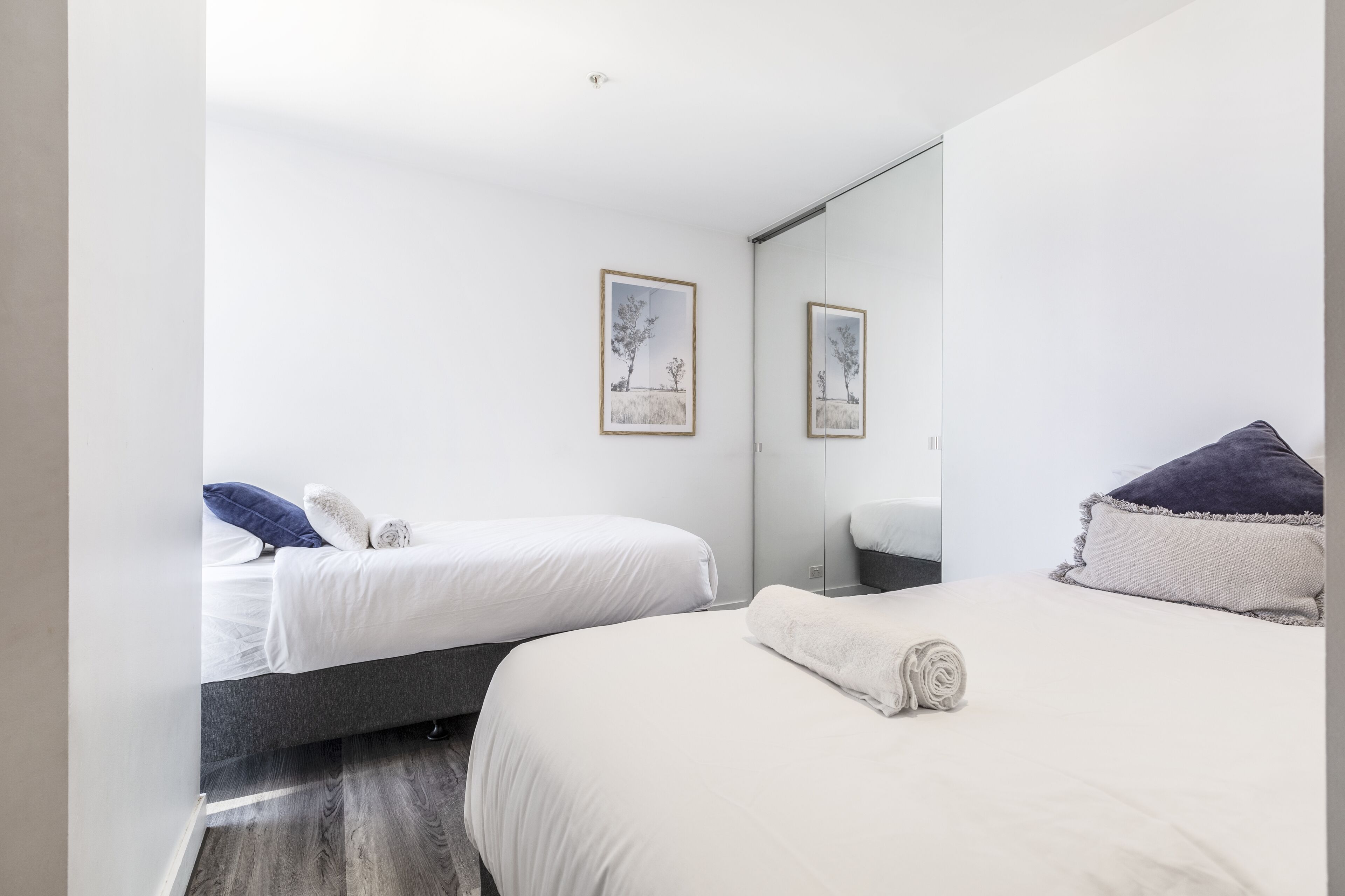 A modern hotel room with two beds, a large mirror, and artwork on the walls.