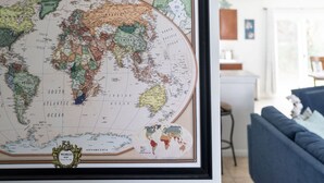 Un mapa mundial enmarcado con un borde decorativo, situado en una habitación con un sofá azul y una pequeña mesa al fondo.