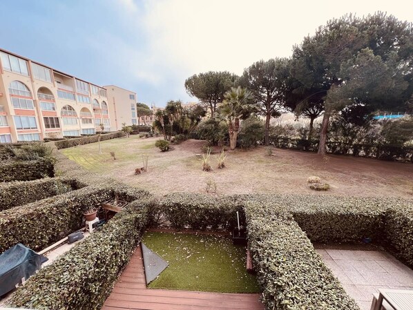A courtyard with neatly trimmed hedges, a small grassy area, and a variety of trees. - Nice 2 room with cabin swimming pool Richelieu Cap d'Agde (LE CAP D AGDE)