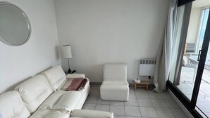 En moderne stue med en hvid sofa, en hvid lænestol og et lille bord. Et stort vindue giver naturligt lys og udsigt udend ørs.