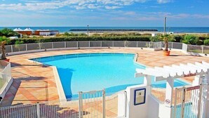 En swimmingpool med buet kant, omgivet af et hvidt hegn, og havudsigt i baggrunden.