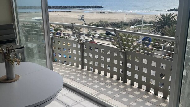 En balkon med udsigt over stranden, et bord og stole.