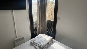 Et hotelværelse med seng, et vægmonteret fladskærms-tv og et vindue med gardiner.