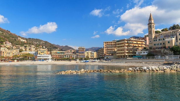 A coastal town with a prominent tower, a beach, and buildings with balconies.