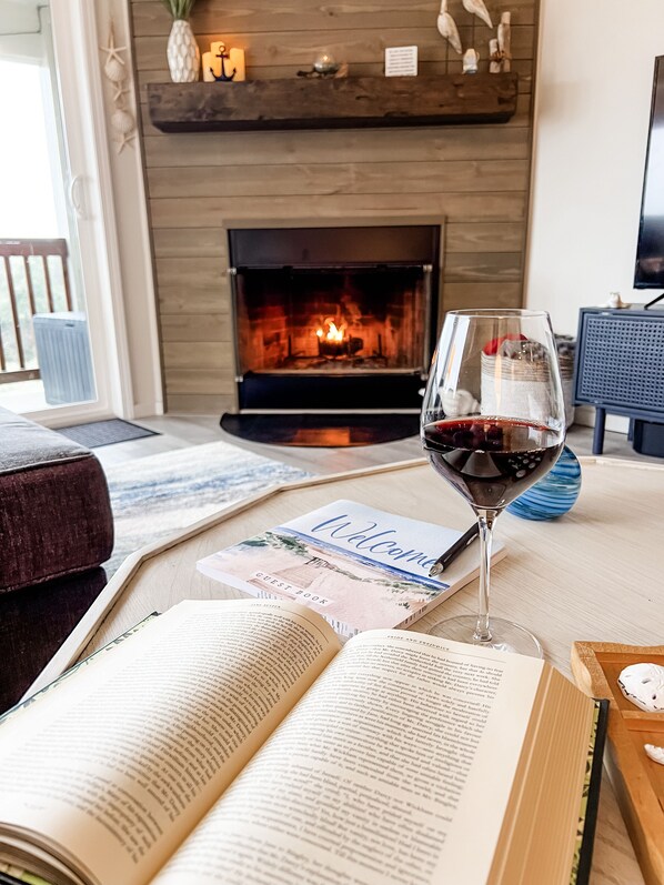 Una sala de estar acogedora con chimenea, una copa de vino tinto y un libro de visitas sobre una mesa.