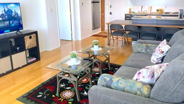 A modern living room with a sofa, glass coffee table, and a TV. There is a kitchen area with a refrigerator, microwave, and cabinets. - Entire apartment 10 min from Clearwater Beach
 (Clearwater)