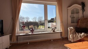 Ein Zimmer mit großem Fenster, Heizkörper, Fernseher und Schrank.