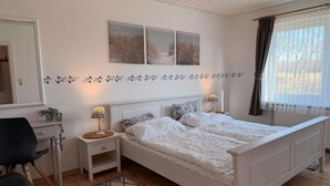 Ein Schlafzimmer mit einem Doppelbett, zwei Nachttischen, einem Sessel, einem Spiegel und einem fenster mit Vorhängen.