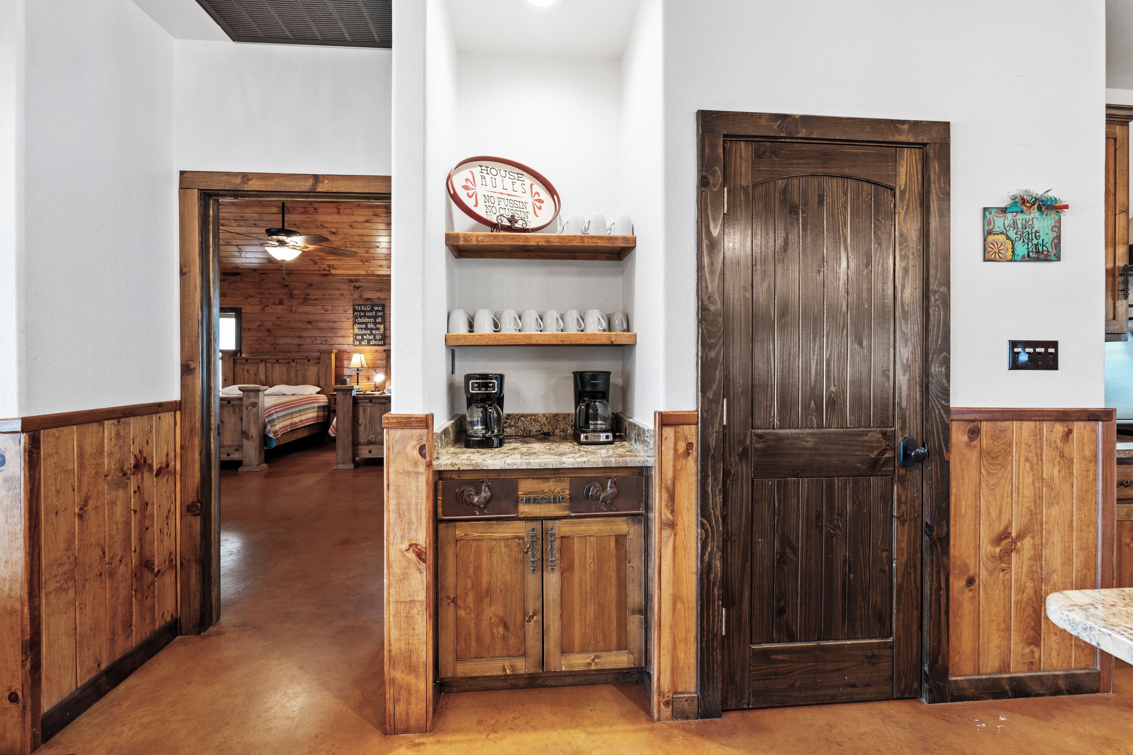 A wooden hallway with a kitchen area featuring a coffee maker and shelves.