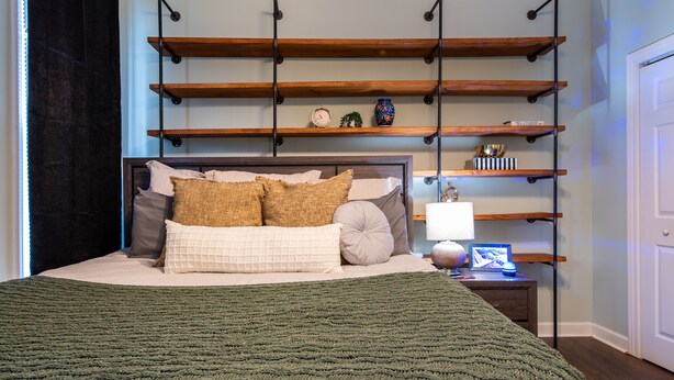 A neatly arranged bedroom with a bed, pillows, a bedside table with a lamp, and shelves above the bed. - Cozy pet-friendly home with fenced backyard, fully equipped for long-term stays. (Louisville)