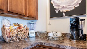 A kitchen with wooden cabinets, a blender, a coffee maker, and a basket of snacks. - Cozy pet-friendly home with fenced backyard, fully equipped for long-term stays. (Louisville)