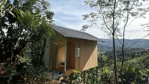 A wooden cabin with a sloped roof, surrounded by lush greenery and a view of distant hills. - Midori Coffee Farm (Nam Ban Lam Ha)