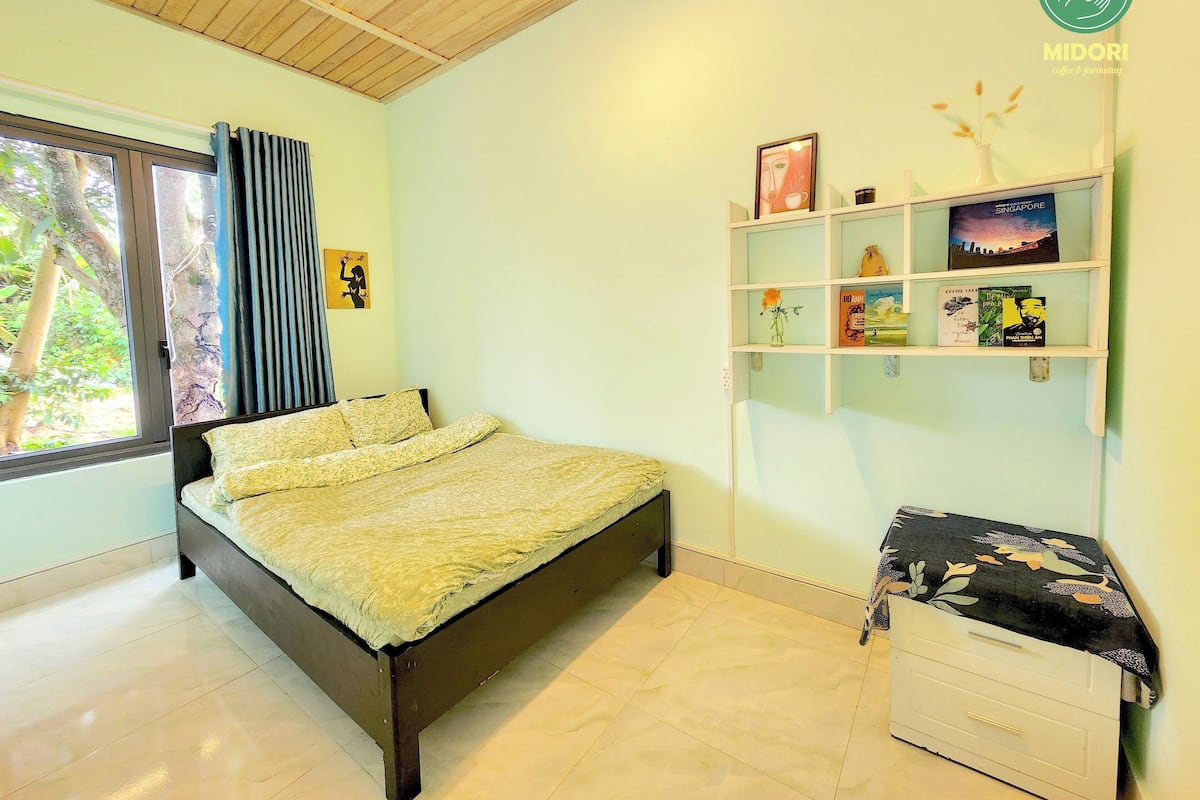 A bedroom with a bed, a window with curtains, a shelf with books and decorative items, and a white dresser.
