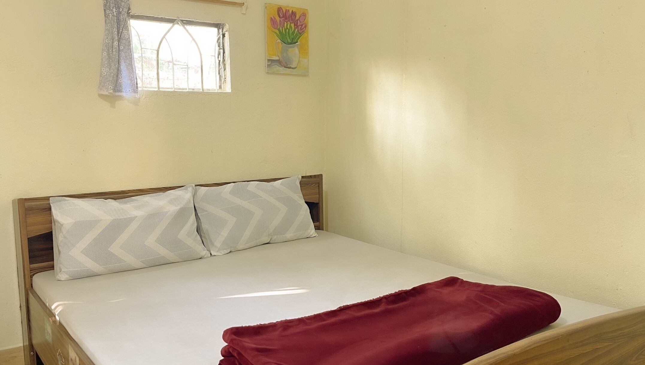 Un lit simple avec une tête de lit en bois, deux oreillers et une couverture rouge.