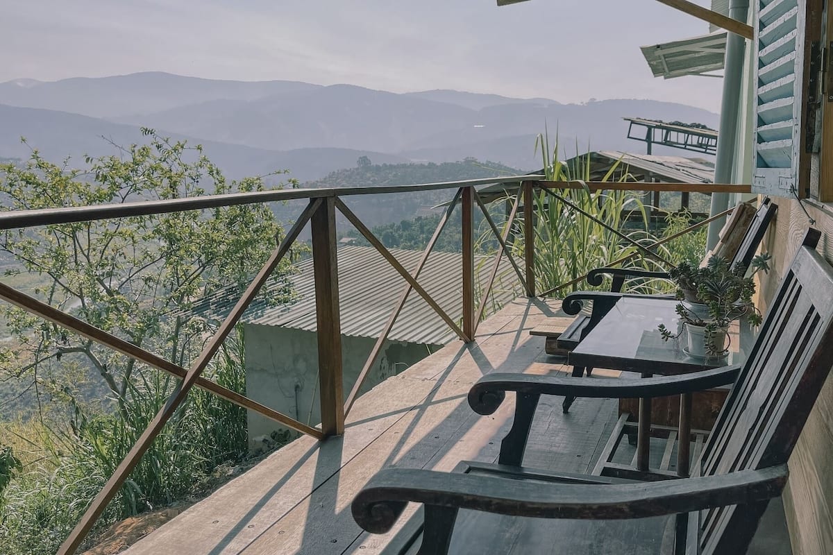 A balcony with a view of distant mountains, a wooden bench, and a potted plant.