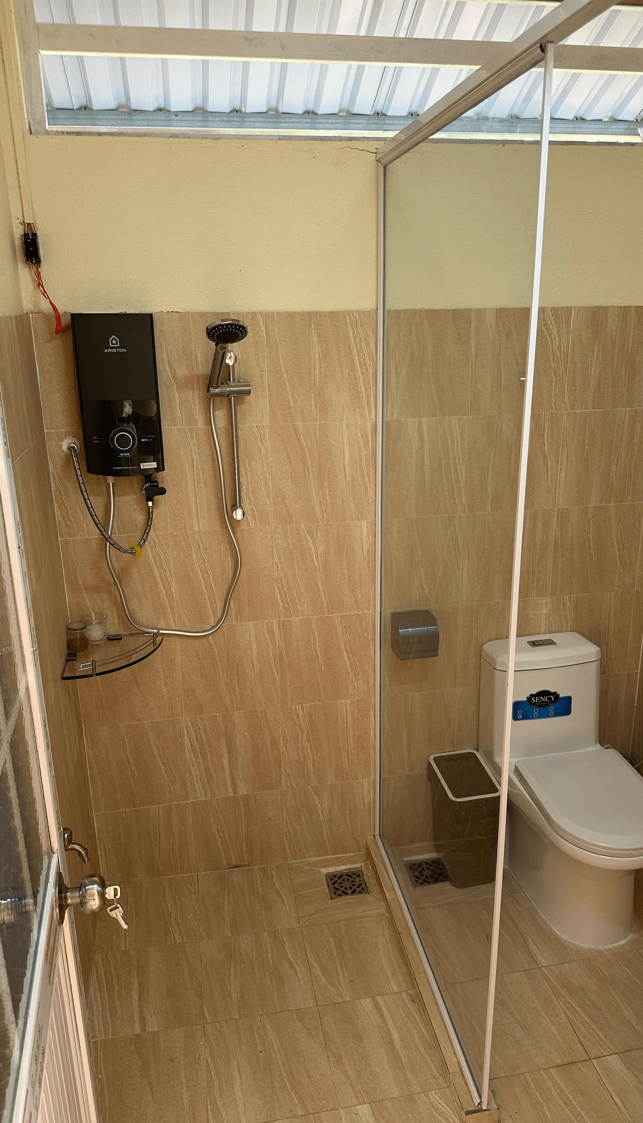 A shower area with a glass door, a control panel, and a toilet with a blue sign.