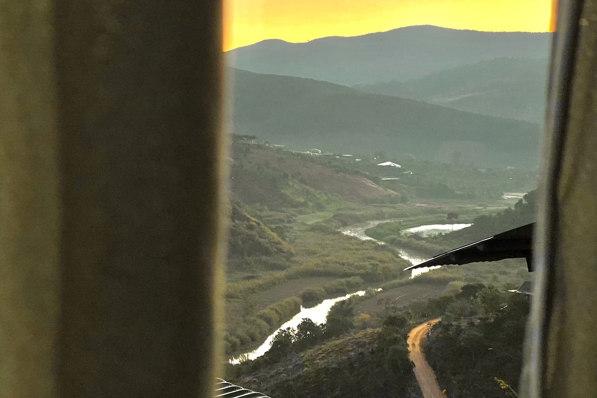 A view from a window overlooking a river, surrounded by hills and a road.
