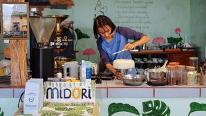 A person preparing food at a counter with a coffee machine, jars, and a sign reading "MIDORI". - Midori Coffee Farm (Nam Ban Lam Ha)