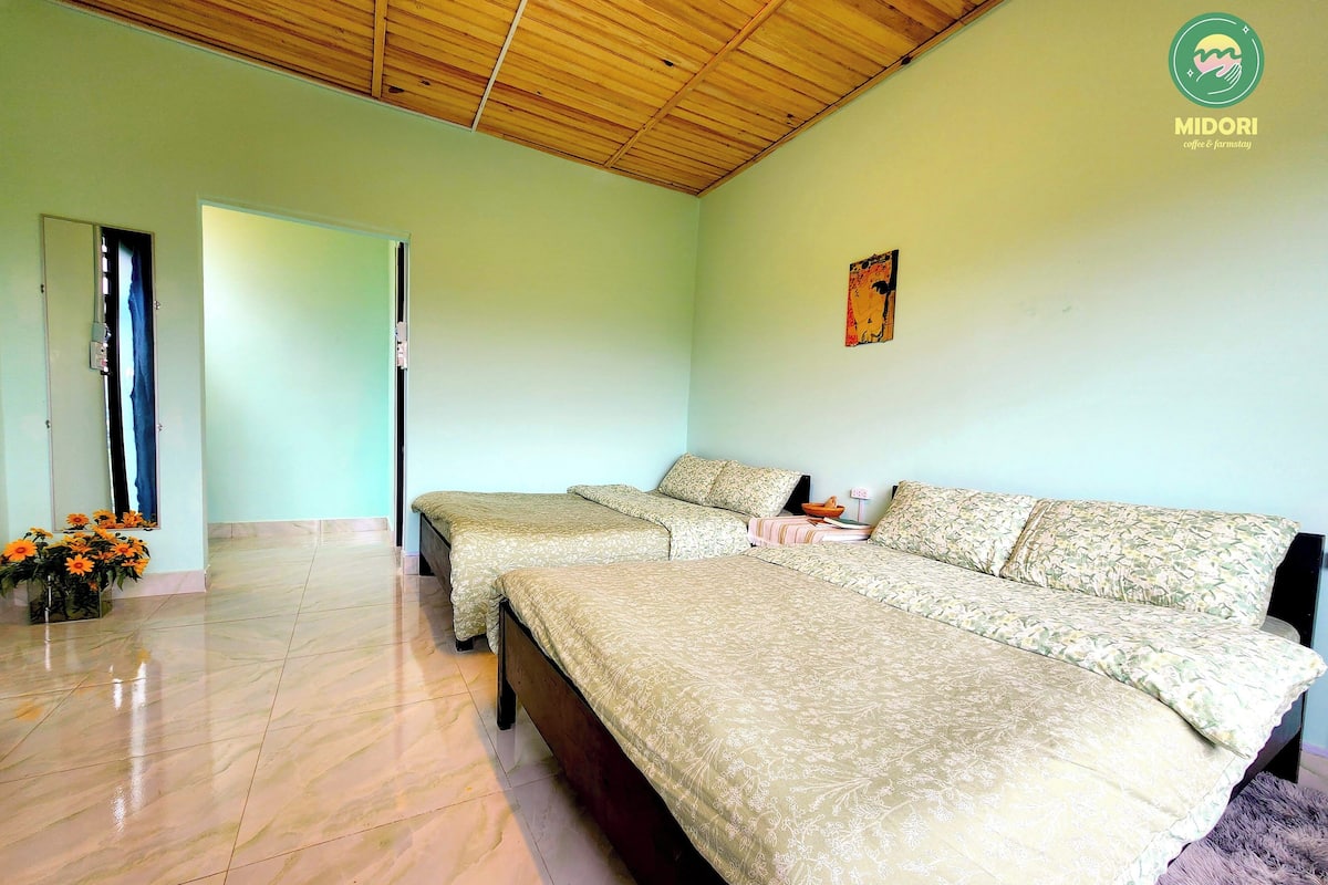 A room with a wooden ceiling, a bed with floral bedding, a small table, and a vase with flowers.