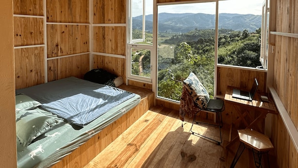 A wooden room with a bed, a desk, and a large window offering a view of the countryside. - Midori Coffee Farm (Nam Ban Lam Ha)