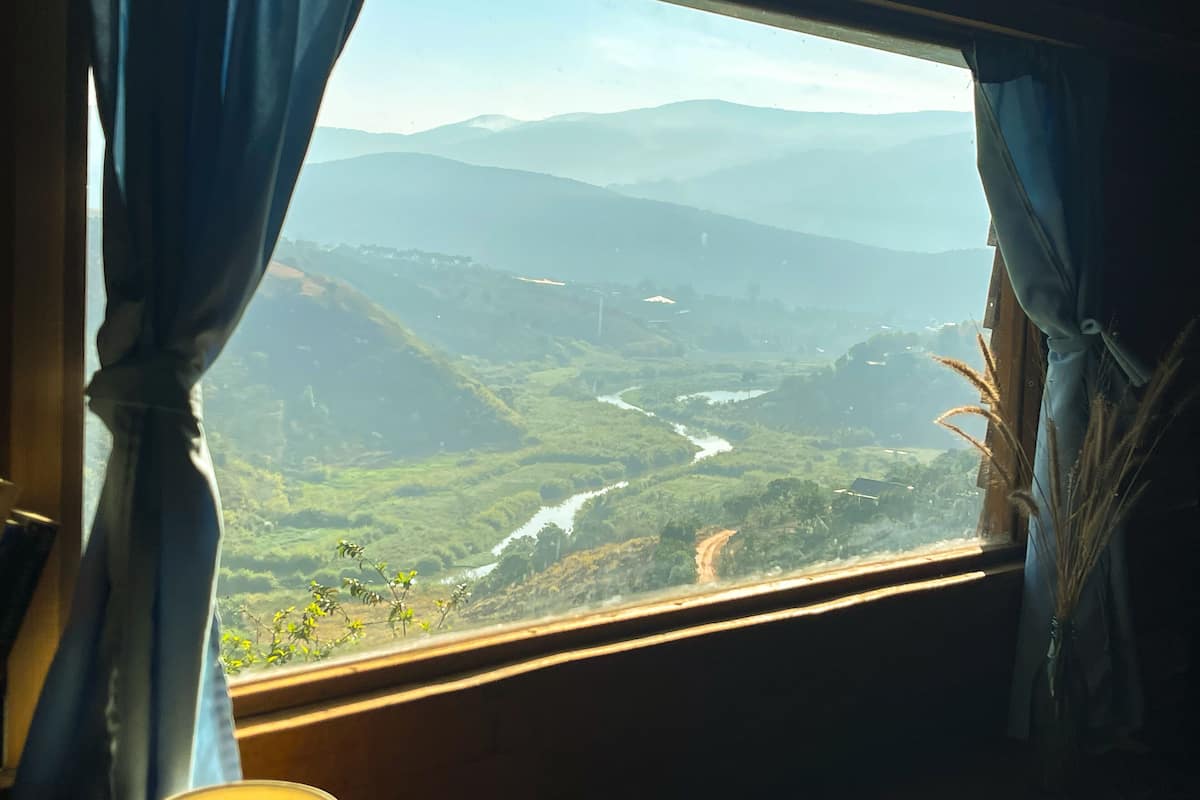 A window view of a valley with a river, surrounded by hills.