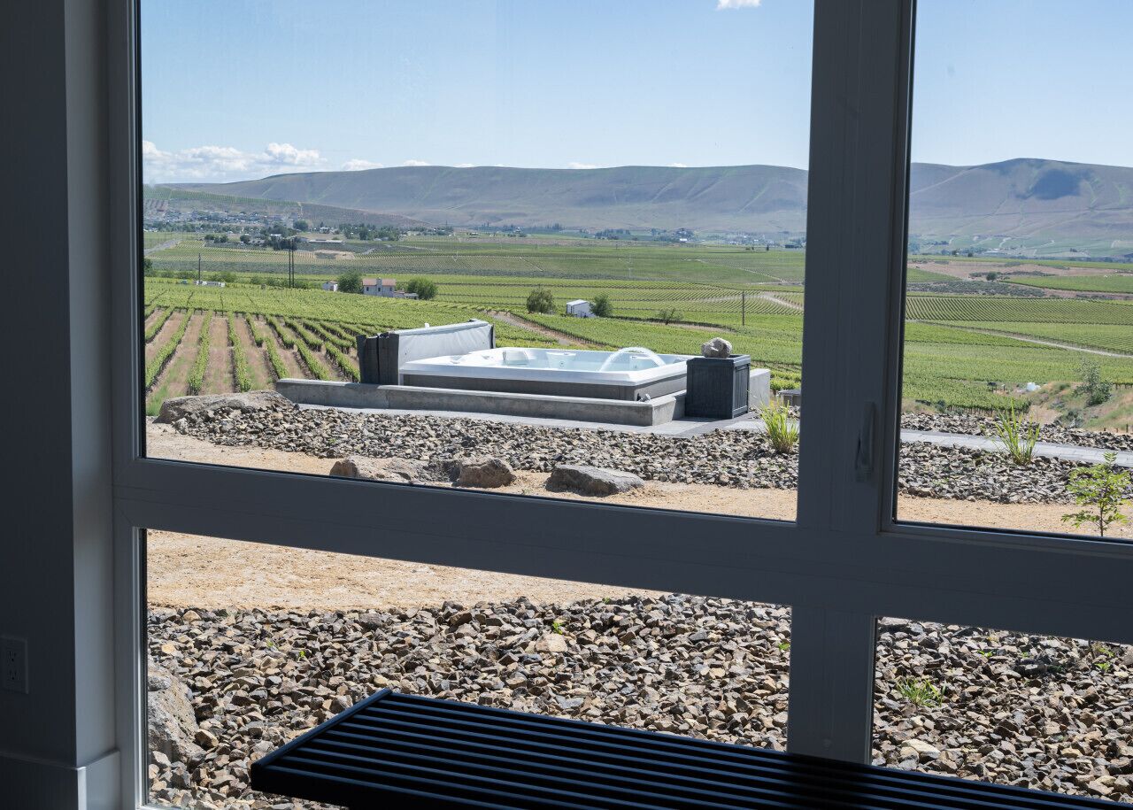 Vista a través de una ventana que muestra un paisaje de viñedos con una zona de estar exterior moderna.