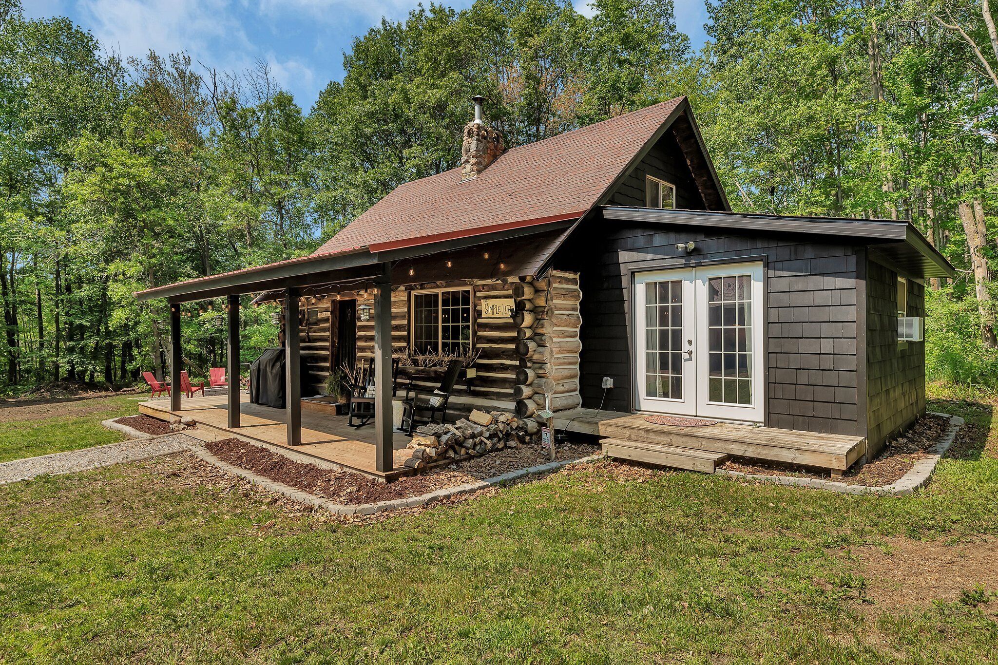 A log cabin with a covered porch, a chimney, and a deck area with outdoor seating.