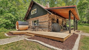 Una cabaña de troncos con terraza, mobiliario exterior y zona de barbacoa.