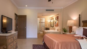 A hotel room with a bed, a television, a desk with a lamp, a bathroom with a sink and mirror, and a door leading to another room. - All-Inclusive ocean front resort in Cabo San Lucas! Walkable to downtown Cabo! (Cabo San Lucas)