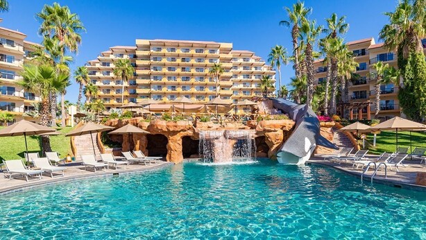 A hotel pool with a waterfall feature, lounge chairs, and palm trees. - All-Inclusive ocean front resort in Cabo San Lucas! Walkable to downtown Cabo! (Cabo San Lucas)