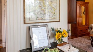 A room with a framed map, a framed invitation, and a vase with sunflowers on a table. - Charming 2 Bedroom Sunday Haus•1 Block to Main St•Quiet Perfectly Located Gem! (Fredericksburg)