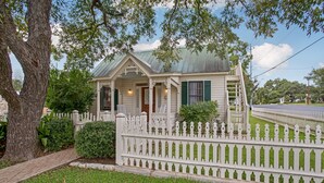 A single-story house with a porch, a picket fence, and a small garden. - Charming 2 Bedroom Sunday Haus•1 Block to Main St•Quiet Perfectly Located Gem! (Fredericksburg)