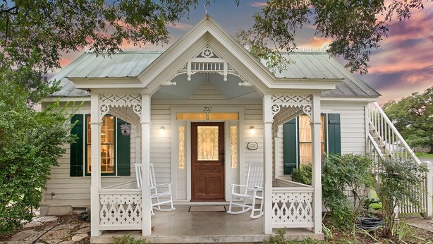 A quaint, single-story house with a porch, a front door, and a staircase leading to the upper level. - Charming 2 Bedroom Sunday Haus•1 Block to Main St•Quiet Perfectly Located Gem! (Fredericksburg)