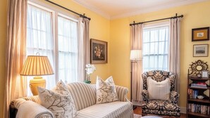 A cozy living room with a striped sofa, a patterned armchair, a small round table, and a bookshelf. - Charming 2 Bedroom Sunday Haus•1 Block to Main St•Quiet Perfectly Located Gem! (Fredericksburg)