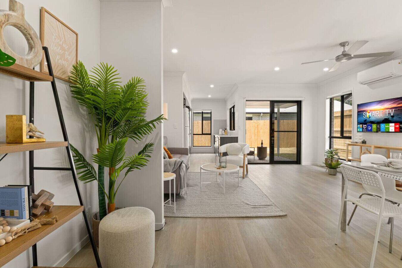 A modern living room with a sofa, coffee table, and chairs, a large plant, and a flat-screen TV.