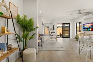 A modern living room with a sofa, coffee table, and chairs, a large plant, and a flat-screen TV.