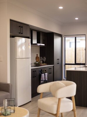 A modern kitchen with dark cabinetry, a white refrigerator, and a dining area with a white chair.