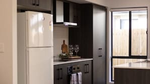 Una cocina moderna con armarios oscuros, un refrigerador blanco y una zona de comedor con una silla blanca.