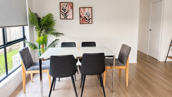 A modern dining area with a glass table, black chairs, and a potted plant.