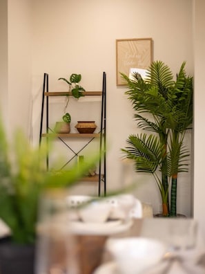 A room with a plant shelf, a framed quote on the wall, and a large potted plant.